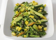 a white plate topped with green beans and corn next to a bowl of dipping sauce