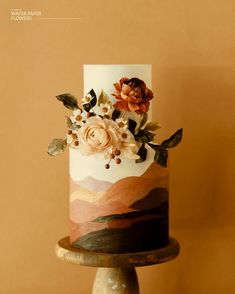 a white and pink cake with flowers on it sitting on top of a wooden stand