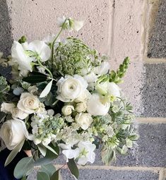 a bouquet of white flowers sitting on top of a table next to a brick wall