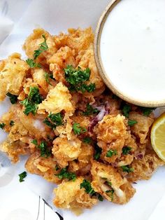 a white plate topped with fried food next to a bowl of ranch dressing and a lemon wedge