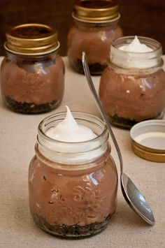 three jars with spoons and some type of dessert in them on a tablecloth