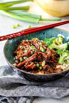 a bowl filled with beef and broccoli next to chopsticks on a table