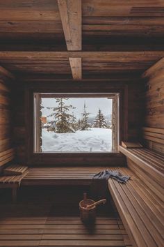 a wooden bench sitting inside of a room next to a large window with snow on the ground