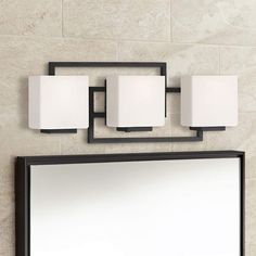 a bathroom mirror with three lights and a light fixture on the wall next to it