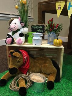 a stuffed cow laying on the ground next to a table with flowers and other items