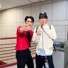 two young men standing next to each other in front of a metal railing with their hands together