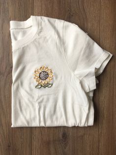 a white t - shirt with a sunflower embroidered on the front and back, sitting on a wooden floor