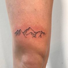 a small tattoo on the leg of a woman with mountains in the background and one behind her