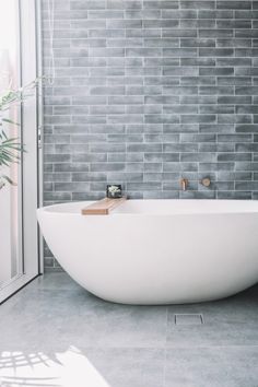 a white bath tub sitting in a bathroom next to a window with a plant on it