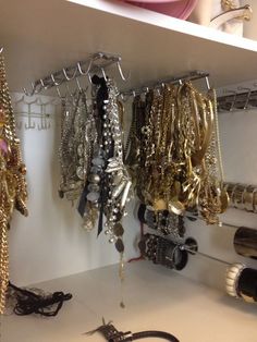 several necklaces and bracelets are hanging on the wall in a closet with white shelving