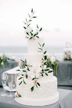 a white wedding cake with flowers and greenery on the top is sitting on a table