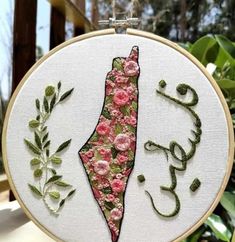 the embroidery is hanging in front of a tree and some leaves with flowers on it