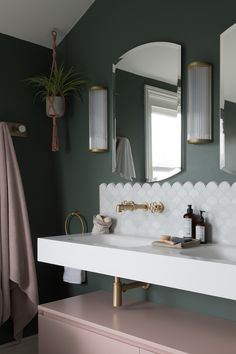 a white sink sitting under a bathroom mirror next to a pink dresser and potted plant