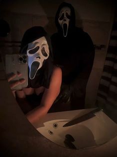 two people with masks on taking a selfie in the bathroom while holding a cell phone