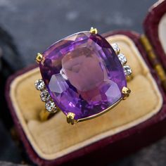 This gorgeous cocktail ring showcases a cushion cut amethyst with a medium-deep hue and lively light return.  The amethyst is accented on each side with three bright diamonds. We love this classic cocktail ring design. The ring is crafted in 14k yellow gold and is currently a size 7. Luxury Diamond Amethyst Ring With Halo Setting, Luxury Cushion Cut Amethyst Ring With Accent Stones, Purple Cushion Ring, Luxury Gold Round Amethyst Ring, Luxury Large Oval Amethyst Ring, Luxury Yellow Gold Amethyst Ring With Accent Stones, Luxury Elegant Amethyst Ring With Large Stone, Luxury Cabochon Amethyst Engagement Ring, Luxury Formal Amethyst Ring, Oval Cabochon