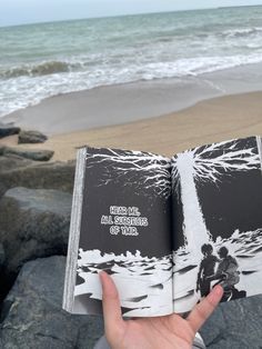 someone is holding an open book on the beach