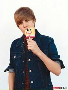 a boy in a denim jacket is holding a cookie and looking at the camera with his mouth open