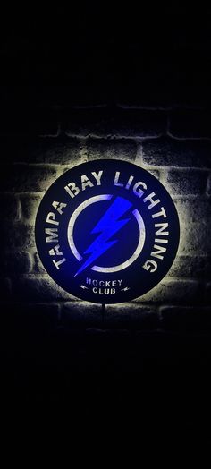 the tampa bay lightning logo is lit up on a brick wall in front of it