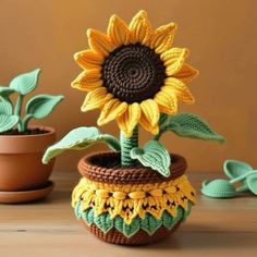 a crocheted sunflower sitting in a pot next to two small pots filled with plants