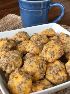 a white bowl filled with muffins next to a blue mug on a table