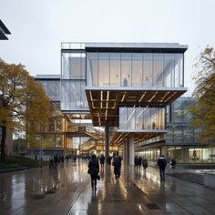 people are walking around in front of a building with glass walls and lights on it