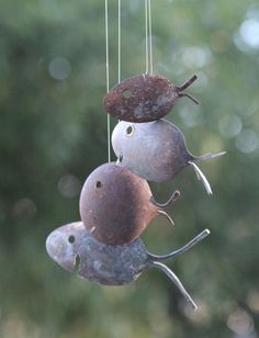 three metal birds hanging from strings in front of trees