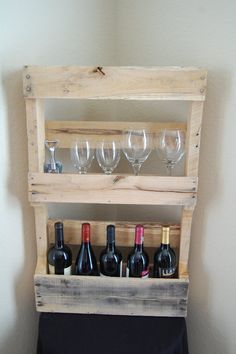 wine glasses and bottles are sitting on a wooden shelf in front of a white wall