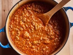 a wooden spoon in a pot filled with chili and meat sauce on top of a table