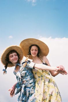 two young women wearing hats and dresses are posing for the camera with their arms around each other