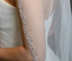 a woman wearing a white wedding dress and holding her arm with silver sequins on it