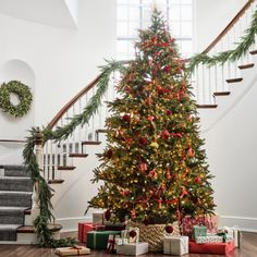 a decorated christmas tree with presents under the banister and stairs in front of it