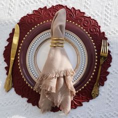 a place setting with napkins, fork and knife on a red plate decorated with gold trim