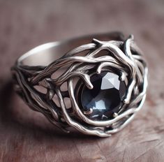 a silver ring with a black stone in it on top of a wooden table next to a piece of wood