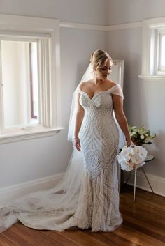 a woman in a wedding dress standing by a window