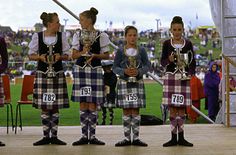 four girls in kilts are holding trophies and posing for the camera