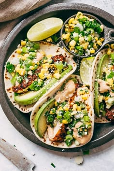 three fish tacos with avocado, corn and cilantro on a plate