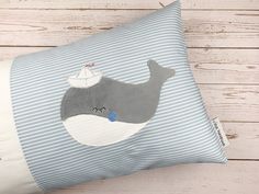 a blue and white striped pillow with a whale on it's side sitting on a wooden floor