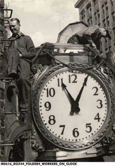 an old black and white photo of two men standing on top of a large clock