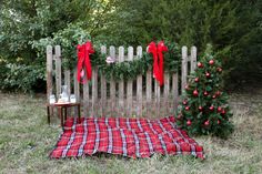 a small christmas tree sitting on top of a blanket next to a wooden fence with red bows