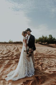 a bride and groom standing in the sand