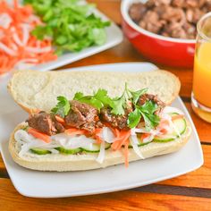 a sandwich with meat, lettuce and carrots next to a glass of orange juice