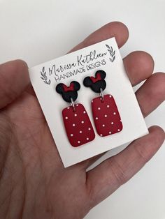 a hand holding a pair of red and white mickey mouse earring earrings on top of a card