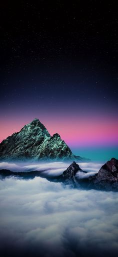 the mountains are covered in clouds under a purple and blue sky with stars above them