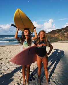 two girls are standing on the beach with surfboards