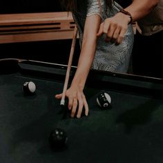 a woman leaning over a pool table with her hand on the cue in front of it