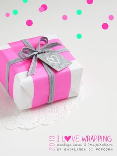 a pink and white gift box with a bow on it sitting on a doily