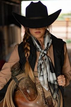 a woman wearing a cowboy hat and holding a saddle