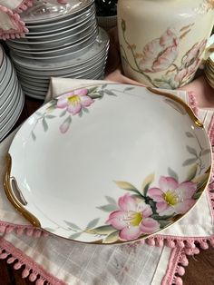 a white plate with pink flowers on it next to stacks of silver plates and dishes