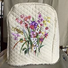 a white quilted chair with flowers painted on the front and back side, sitting on a table