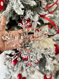 a hand holding a snowflake ornament in front of a christmas tree